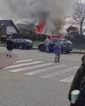 Trzech cywili stoi przed dwoma samochodami na ulicy, w tle dymi i ogień