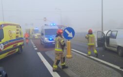 Na jezdni stoi patrol Policji i Ambulans. W tle dwóch strażaków i ratownik medyczny.